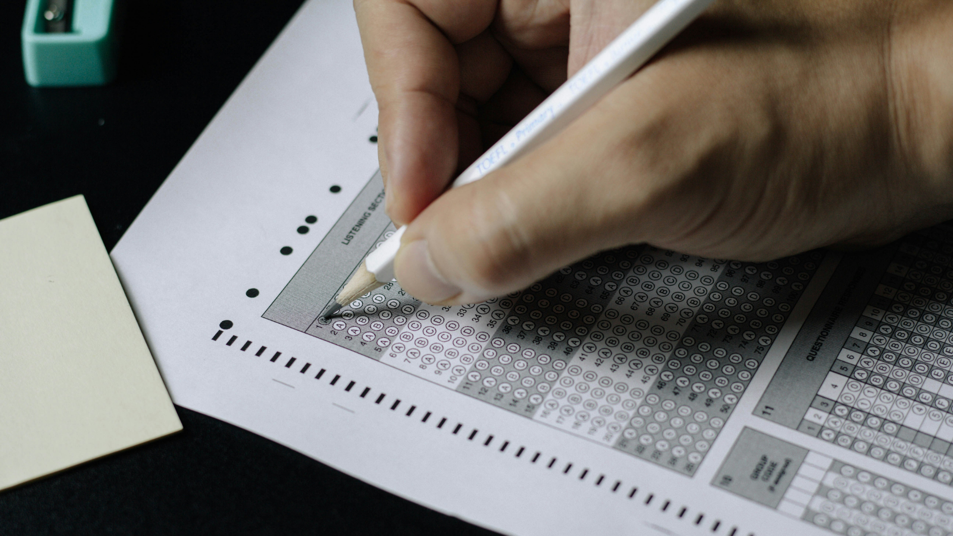 A close up of a hand holding a pencil and filling out a standardized test.