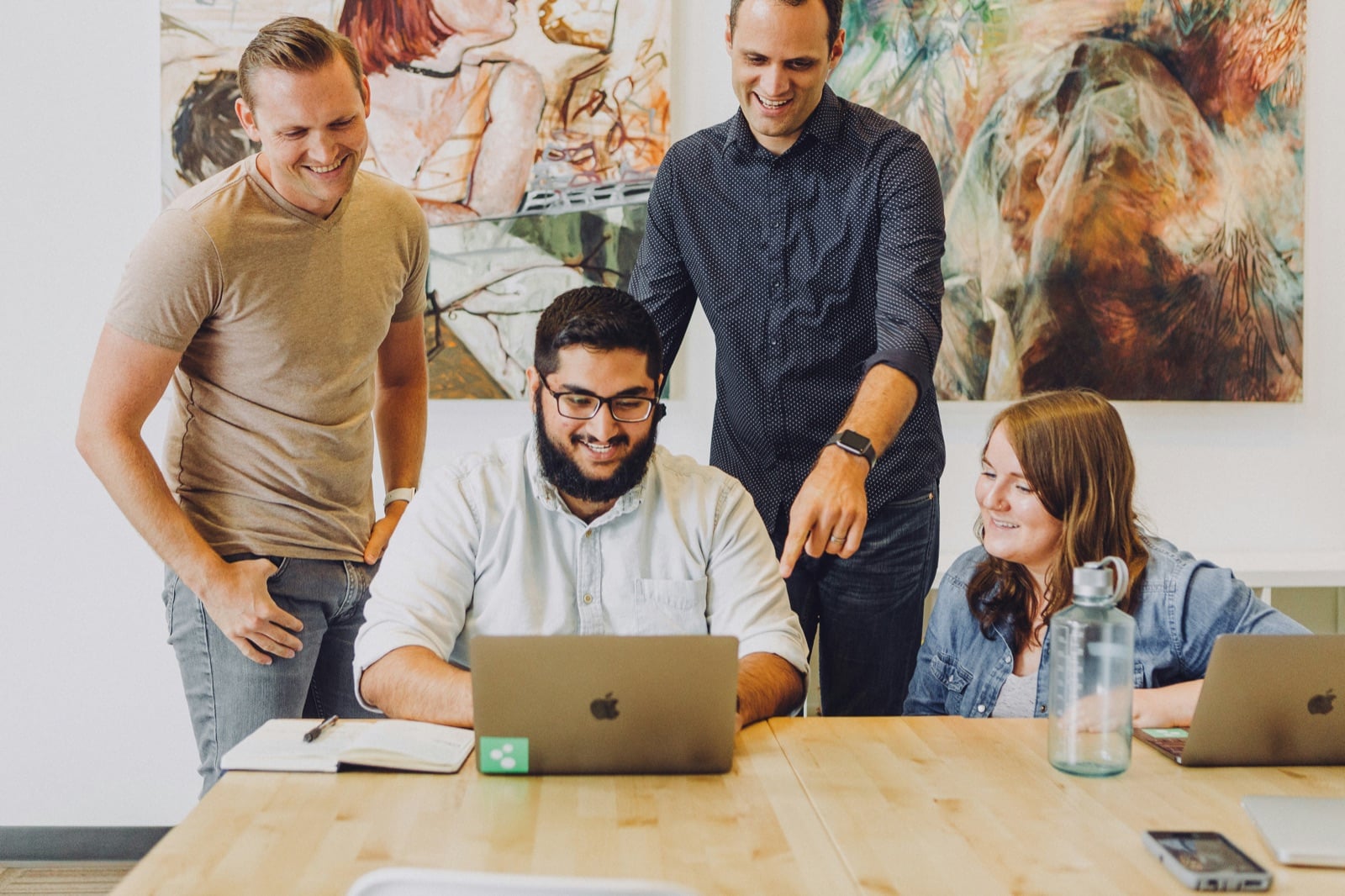 Four coworkers smiling and collaboratively working around a laptop.