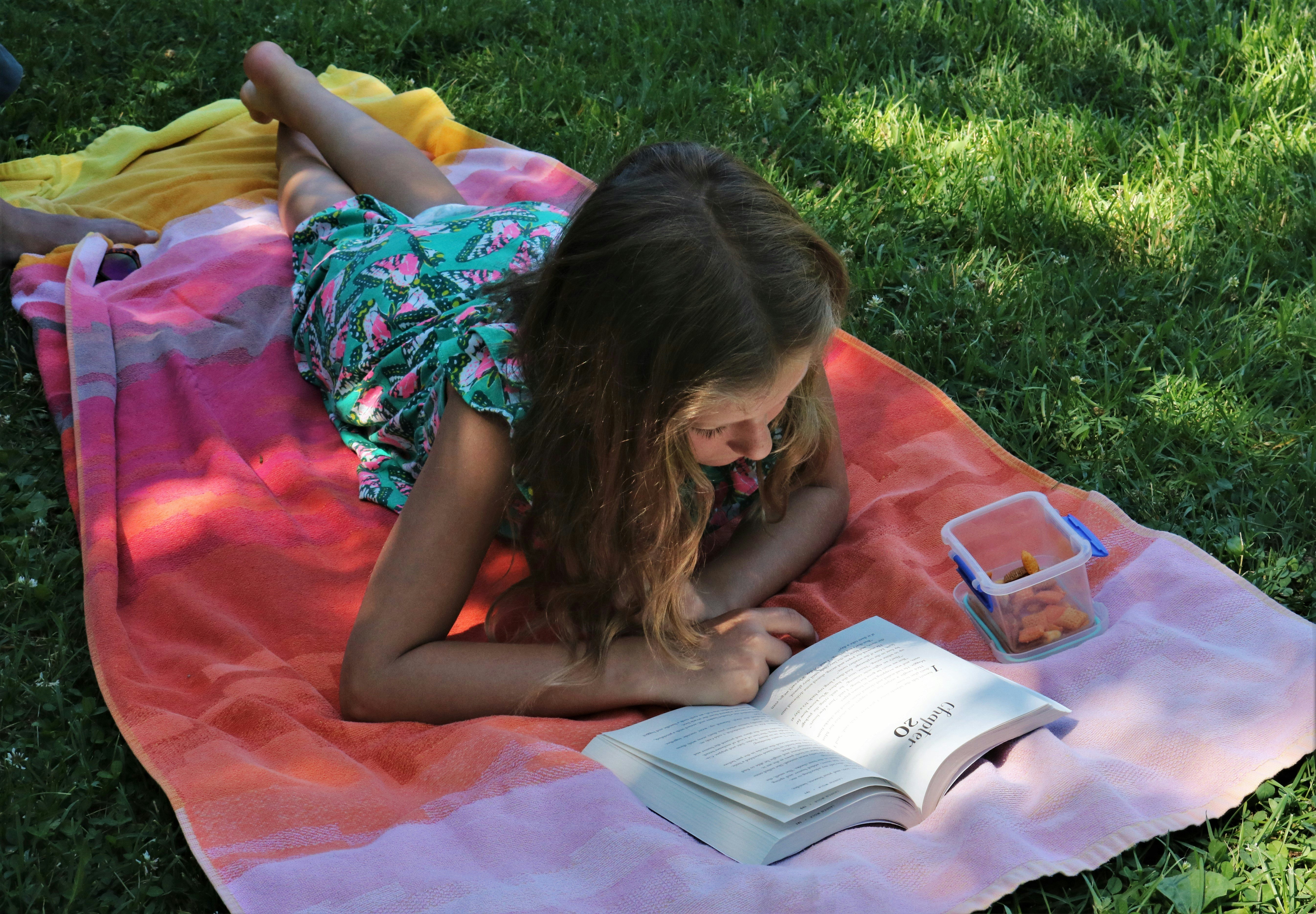 A girl lying on a towel and reading a book outside. Photo courtesy of Skylar Zilka.